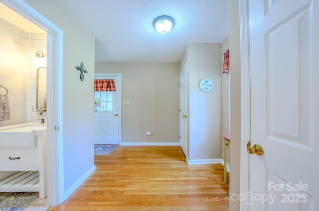 hall featuring sink, light hardwood / wood-style floors, and a textured ceiling