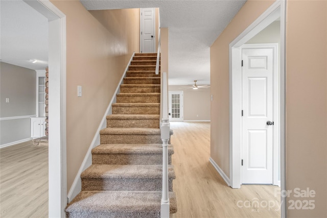 stairway featuring ceiling fan, wood-type flooring, and a textured ceiling