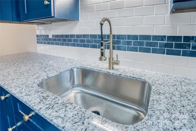 interior details featuring light stone countertops, blue cabinetry, sink, and decorative backsplash