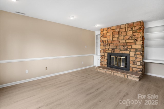 unfurnished living room featuring a stone fireplace, light hardwood / wood-style floors, and built in features