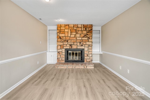 unfurnished living room with light wood-type flooring, a fireplace, and built in shelves