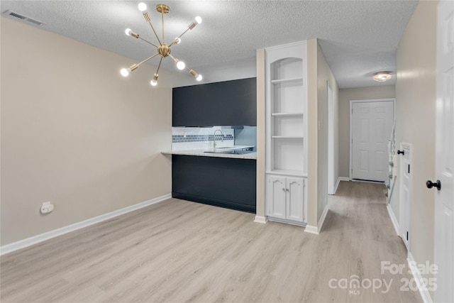 kitchen featuring sink, light hardwood / wood-style flooring, a textured ceiling, an inviting chandelier, and built in shelves