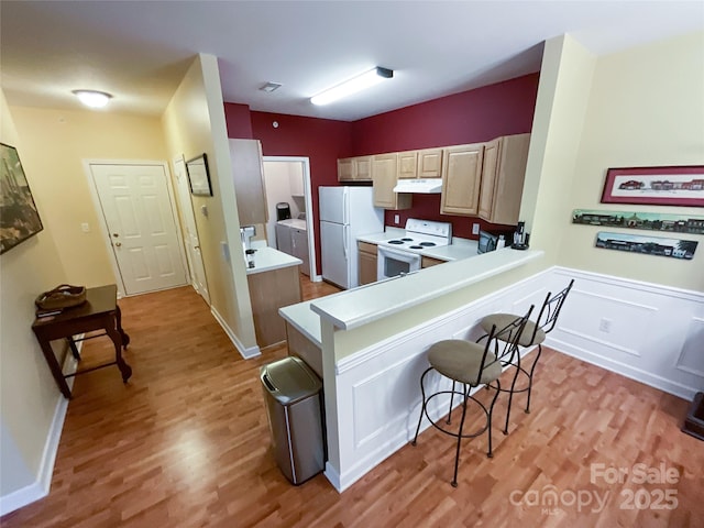 kitchen with white appliances, a kitchen bar, kitchen peninsula, and light hardwood / wood-style floors