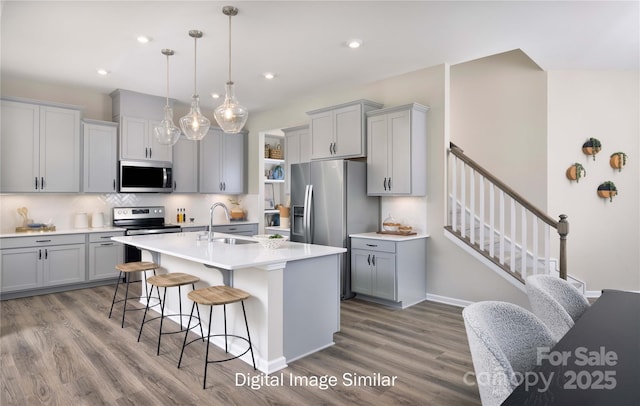 kitchen with sink, appliances with stainless steel finishes, gray cabinetry, hanging light fixtures, and a center island with sink