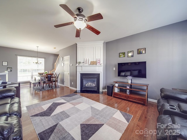 living room with ceiling fan with notable chandelier, wood-type flooring, and a large fireplace