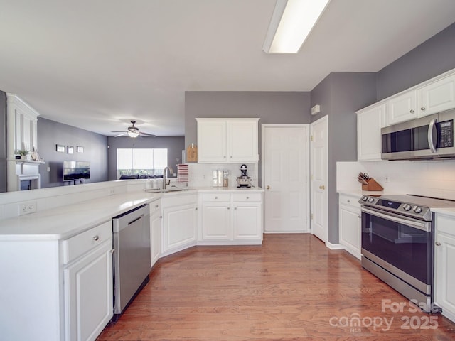 kitchen featuring sink, light hardwood / wood-style flooring, appliances with stainless steel finishes, kitchen peninsula, and white cabinets