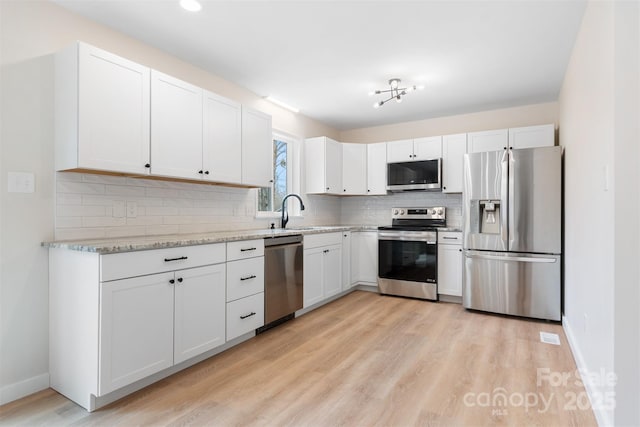 kitchen with light hardwood / wood-style flooring, white cabinetry, backsplash, stainless steel appliances, and light stone countertops