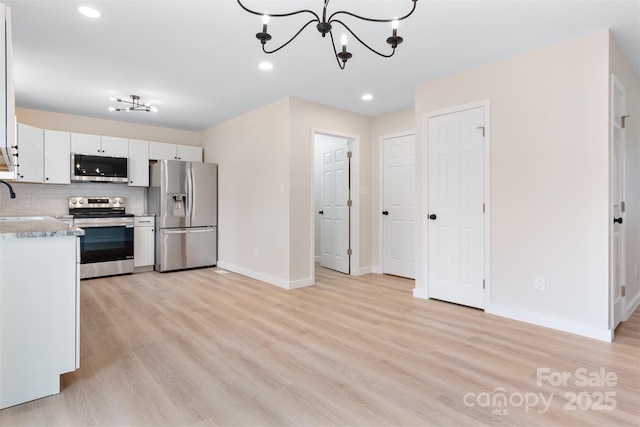 kitchen featuring white cabinetry, light wood-type flooring, backsplash, stainless steel appliances, and an inviting chandelier