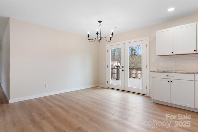 unfurnished dining area featuring a notable chandelier, light hardwood / wood-style floors, and french doors