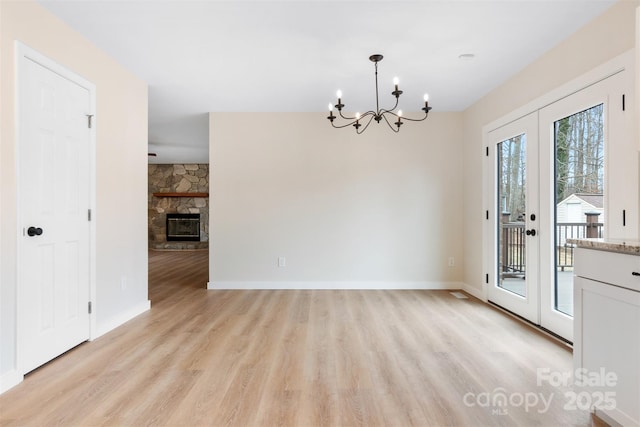 unfurnished dining area with an inviting chandelier, a stone fireplace, french doors, and light wood-type flooring