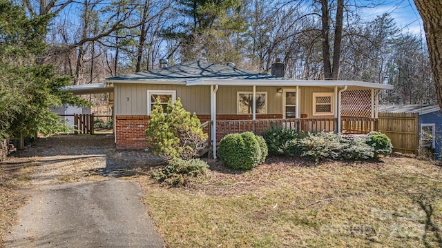 view of front of home featuring a porch, brick siding, driveway, a carport, and a chimney