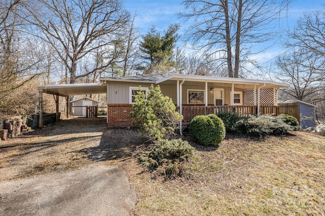 view of front of house featuring covered porch, brick siding, fence, driveway, and a carport