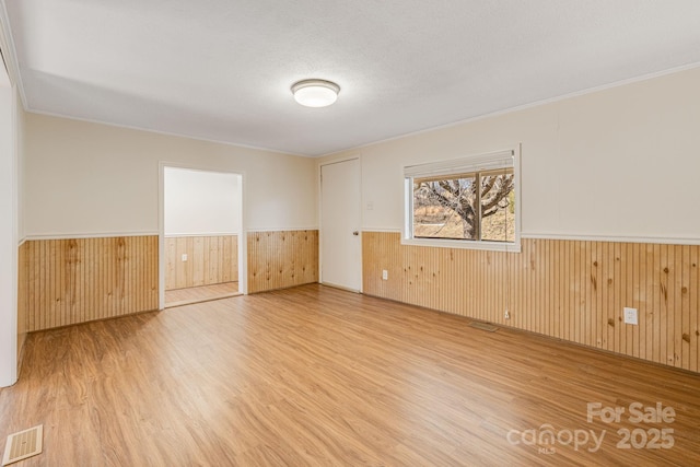 empty room with a wainscoted wall, wooden walls, visible vents, and wood finished floors