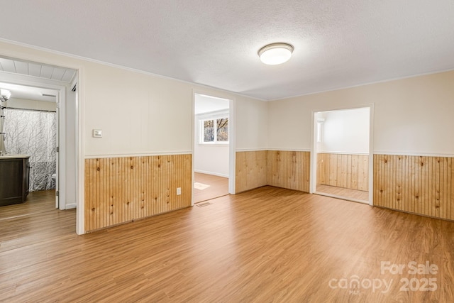 spare room featuring a textured ceiling, wooden walls, a wainscoted wall, wood finished floors, and ornamental molding