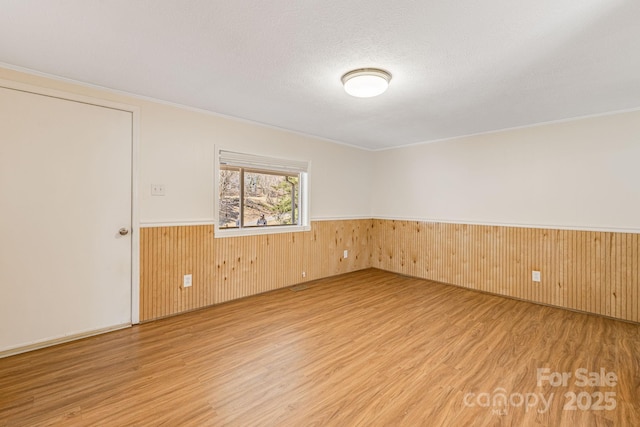 spare room featuring a wainscoted wall, light wood-style flooring, a textured ceiling, and wood walls