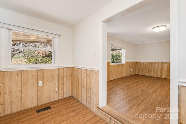 spare room with a wainscoted wall, wooden walls, visible vents, and wood finished floors