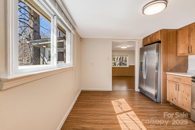 kitchen featuring baseboards, light wood finished floors, stainless steel fridge, and brown cabinets