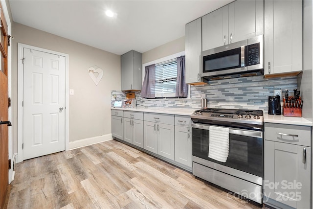 kitchen featuring backsplash, light wood-type flooring, gray cabinets, and appliances with stainless steel finishes