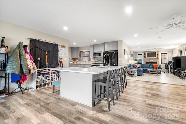 kitchen with tasteful backsplash, a breakfast bar area, a large island with sink, stainless steel appliances, and light hardwood / wood-style flooring