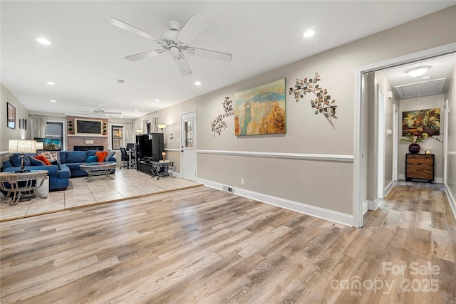 living room featuring a brick fireplace, light hardwood / wood-style flooring, and ceiling fan