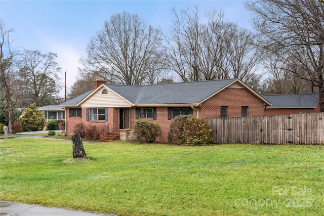 ranch-style house with fence, roof with shingles, a front yard, brick siding, and a chimney