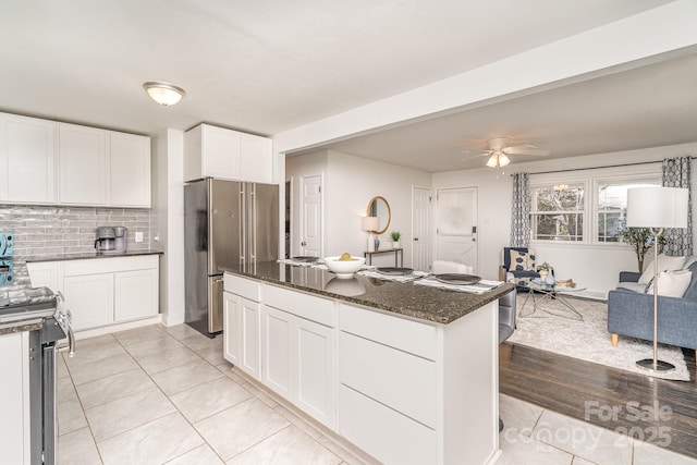 kitchen with light tile patterned floors, stainless steel appliances, white cabinetry, backsplash, and dark stone counters