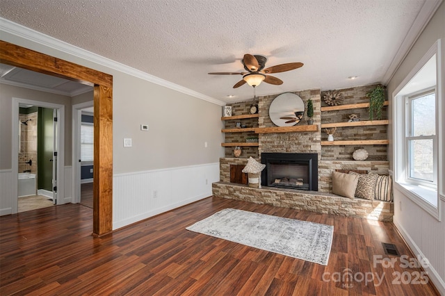 unfurnished living room featuring visible vents, wainscoting, wood finished floors, a textured ceiling, and a stone fireplace