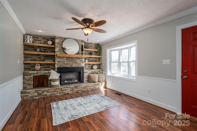 unfurnished living room featuring a wainscoted wall, a stone fireplace, a textured ceiling, and wood finished floors