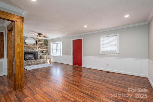 unfurnished living room featuring a textured ceiling, a stone fireplace, wainscoting, and visible vents