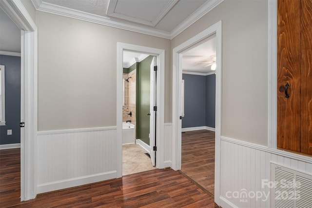 hall with a wainscoted wall, ornamental molding, wood finished floors, and visible vents