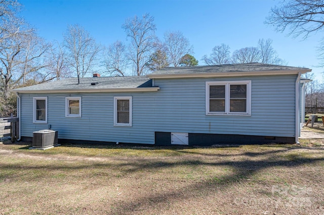 rear view of property featuring cooling unit, crawl space, roof with shingles, and a lawn