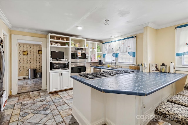 kitchen with appliances with stainless steel finishes, sink, white cabinets, tile counters, and crown molding