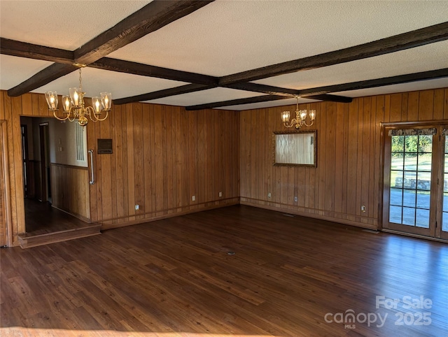 empty room with dark wood-type flooring, a chandelier, a textured ceiling, and beamed ceiling