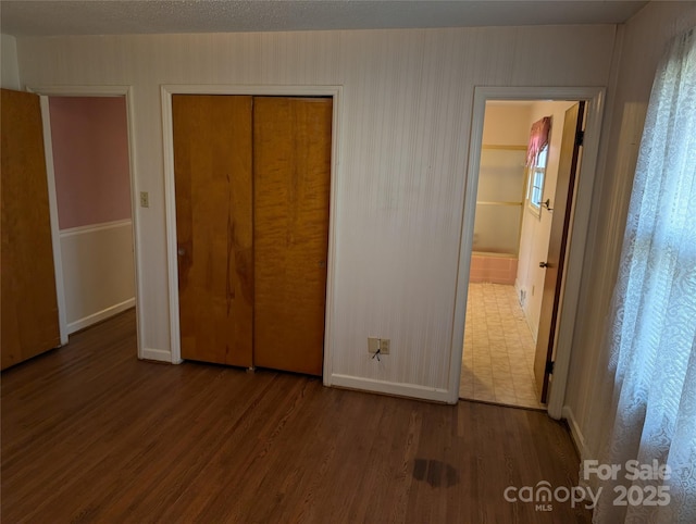 unfurnished bedroom with ensuite bath, wood-type flooring, and a closet