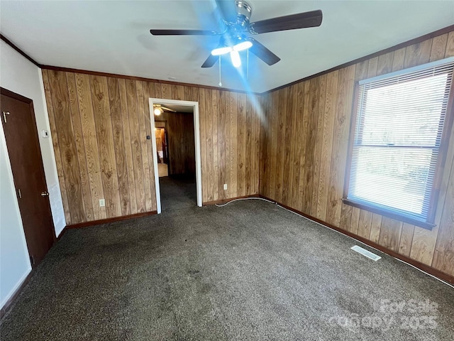 empty room featuring wood walls, ornamental molding, and dark colored carpet