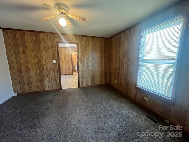 carpeted empty room featuring ornamental molding, ceiling fan, and wood walls