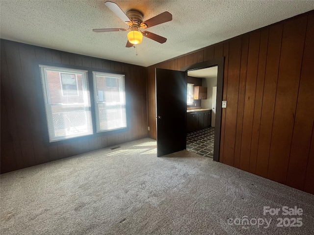 carpeted spare room featuring ceiling fan, a textured ceiling, and wood walls