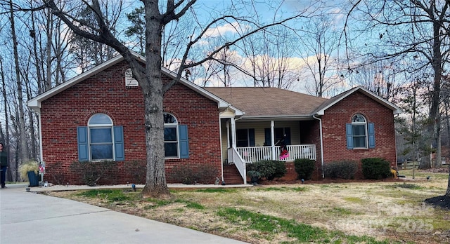 ranch-style home featuring covered porch, brick siding, and roof with shingles