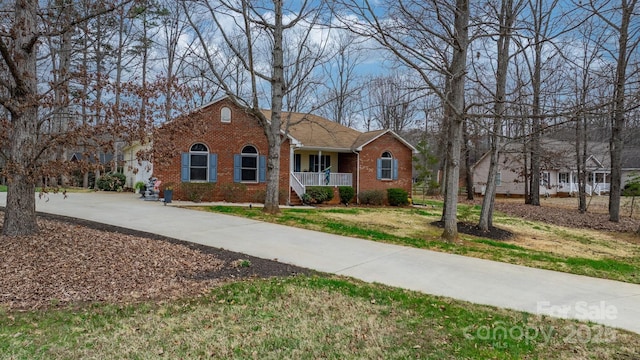 view of front facade with a front yard, a porch, concrete driveway, and brick siding