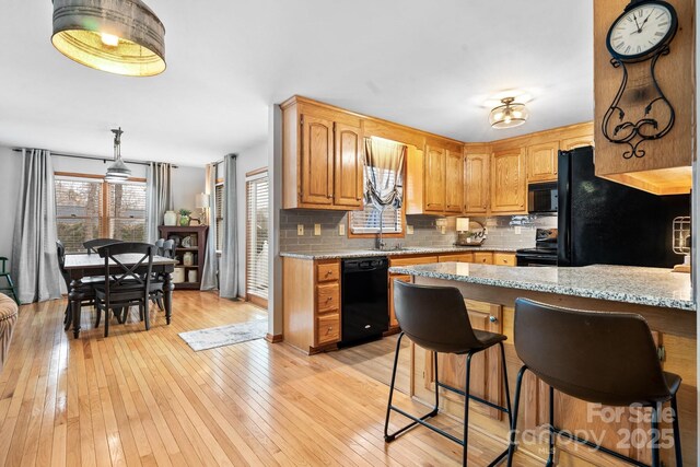 kitchen with light stone counters, decorative backsplash, a sink, light wood-type flooring, and black appliances