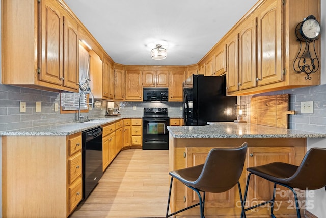 kitchen featuring a peninsula, a sink, light wood-style floors, light stone countertops, and black appliances