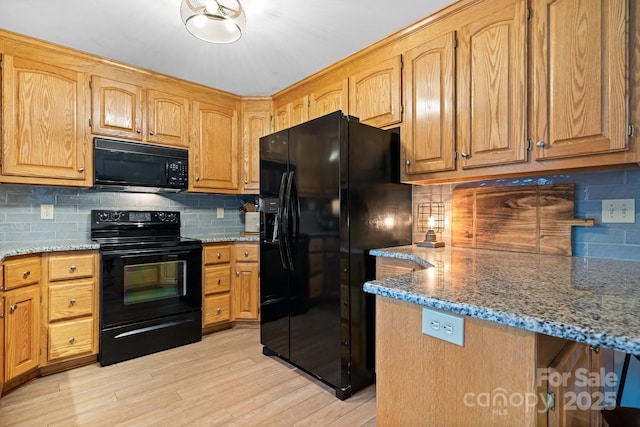 kitchen with black appliances, light stone counters, backsplash, and light wood-style floors