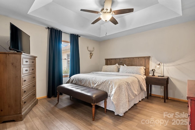 bedroom with light wood-type flooring, a raised ceiling, and baseboards