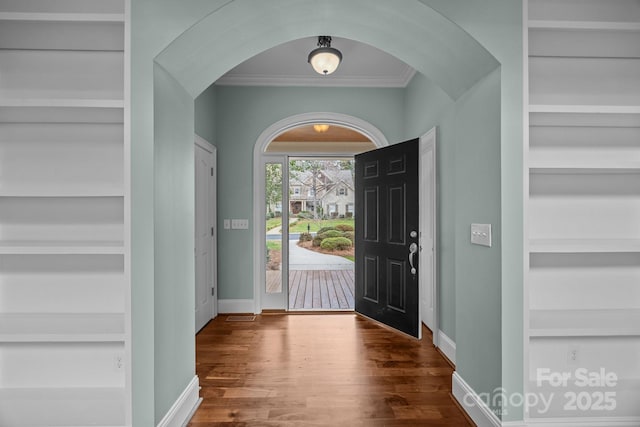 foyer entrance with baseboards, arched walkways, wood finished floors, and ornamental molding