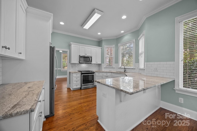 kitchen featuring dark wood-type flooring, tasteful backsplash, appliances with stainless steel finishes, a peninsula, and white cabinets