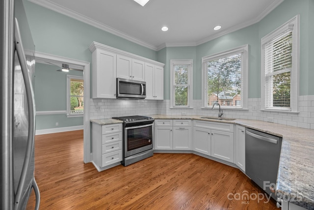 kitchen with a sink, white cabinetry, stainless steel appliances, crown molding, and light wood finished floors