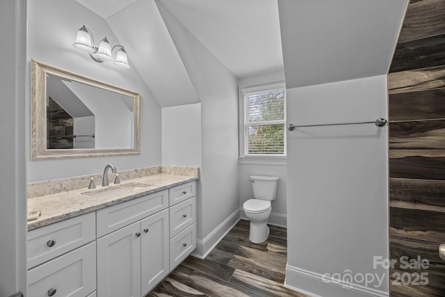 bathroom with toilet, lofted ceiling, wood finished floors, baseboards, and vanity