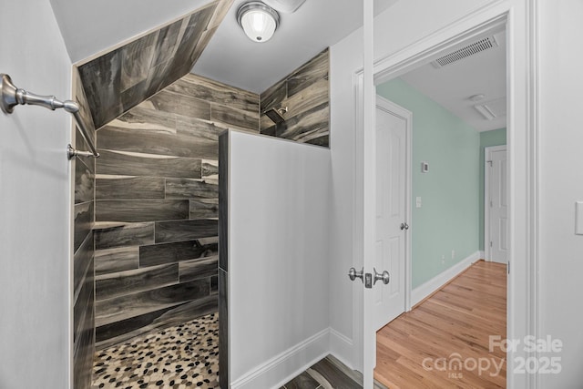 bathroom featuring wood finished floors, a walk in shower, visible vents, and baseboards