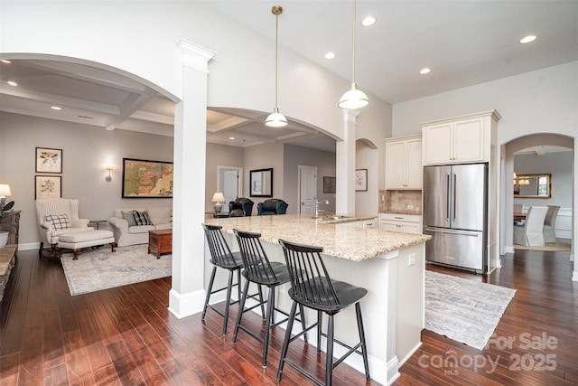 kitchen with light stone counters, arched walkways, open floor plan, high quality fridge, and a kitchen breakfast bar