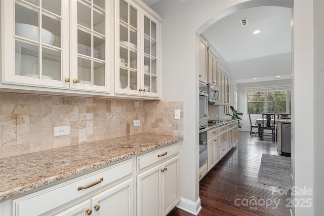 kitchen with arched walkways, dark wood-type flooring, visible vents, appliances with stainless steel finishes, and light stone countertops